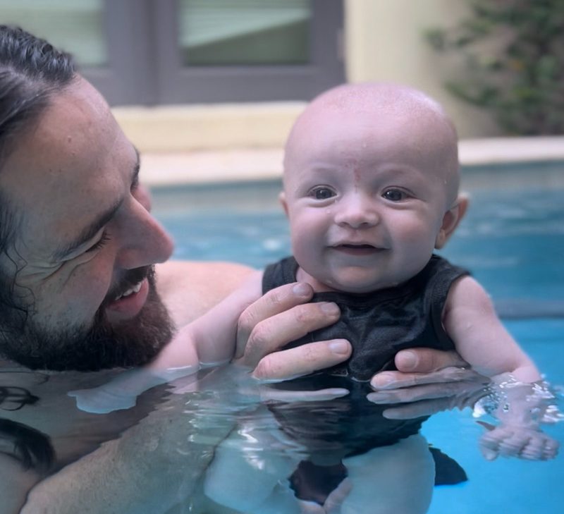 Coach supporting a smiling baby in the water during a parent and toddler lesson
