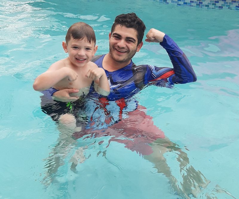 Coach and young swimmer flexing together in the pool