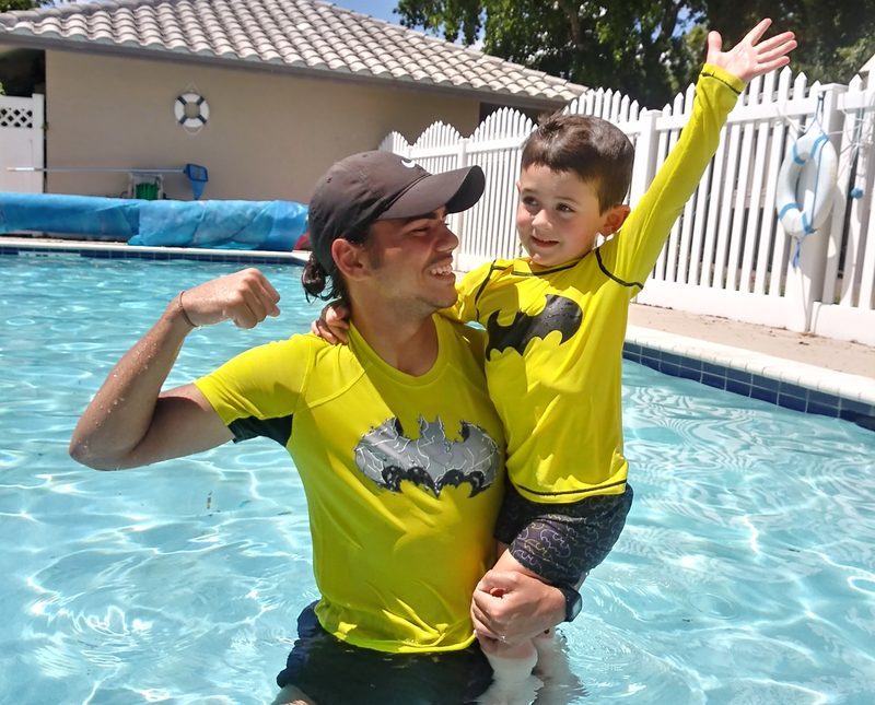Coach in a yellow Superhero Swim shirt lifting a child out of the pool