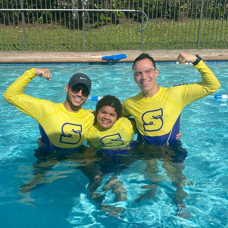 Two Superhero Swim coaches in yellow rash guards in the pool with a young swimmer