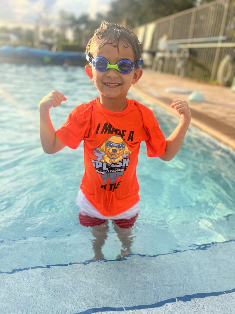 Young swimmer standing in the shallow end flexing