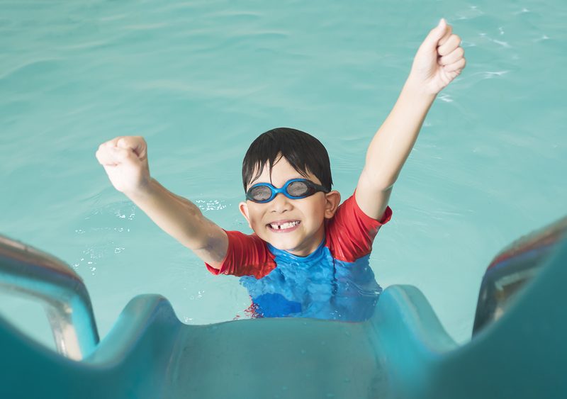 Child coming down a pool slide with arms raised