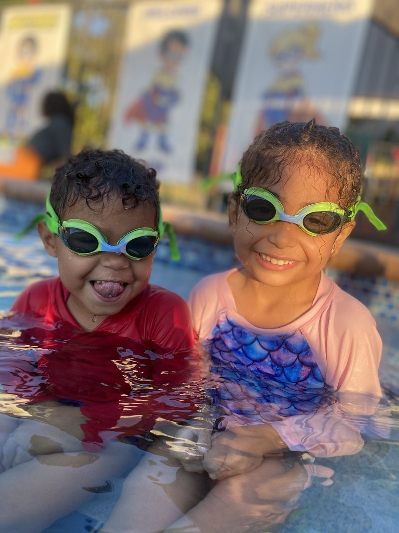 Two children in goggles smiling at the edge of the pool