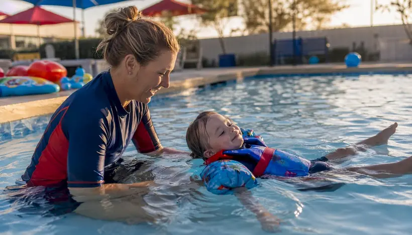 Instructor guiding toddler in outdoor swim pool