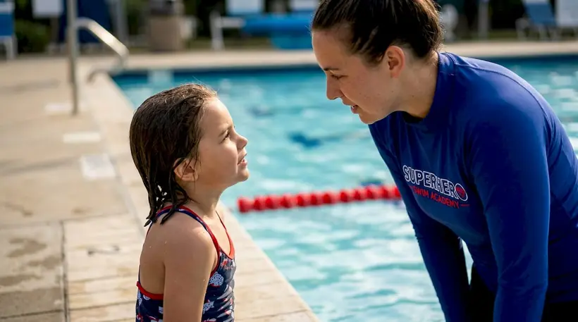 Child at swim lesson poolside listening to instructor