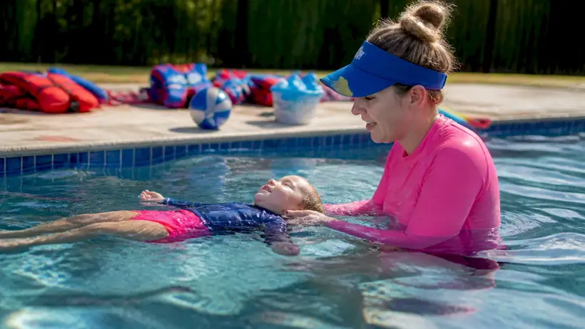 Swim instructor teaching toddler survival float