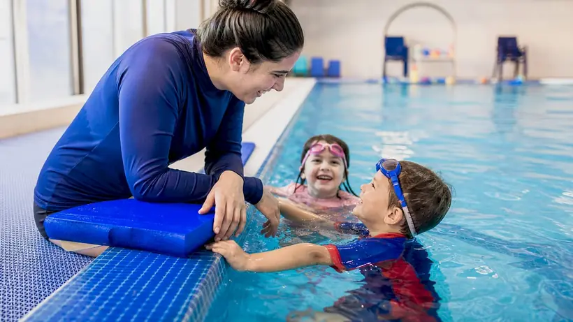 Swim coach correcting girl’s freestyle stroke in pool