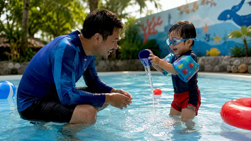Mother encouraging toddler swim class at indoor pool
