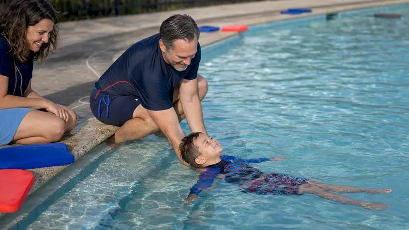 Swim instructor teaching young boy to float