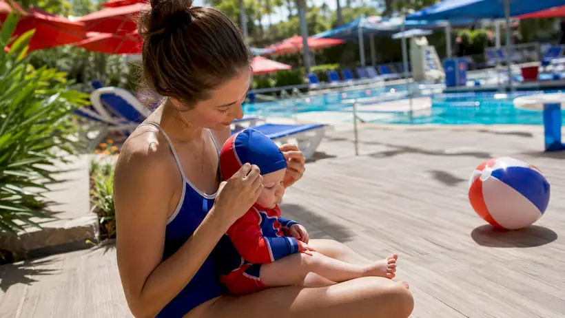 Mother preparing infant for swim lesson poolside