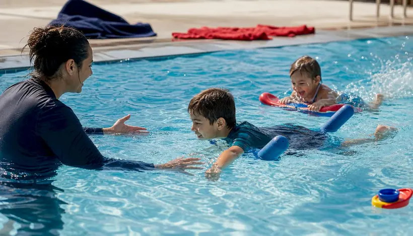 Two siblings swimming with instructor in indoor pool